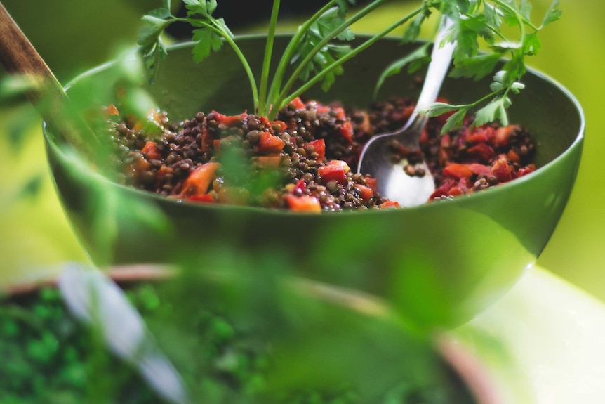 A green bowl filled with legume salad - pieces of tomato are obvious and fresh green herbs are placed in on top.