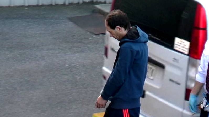 A man in handcuffs walks with his head bowed.