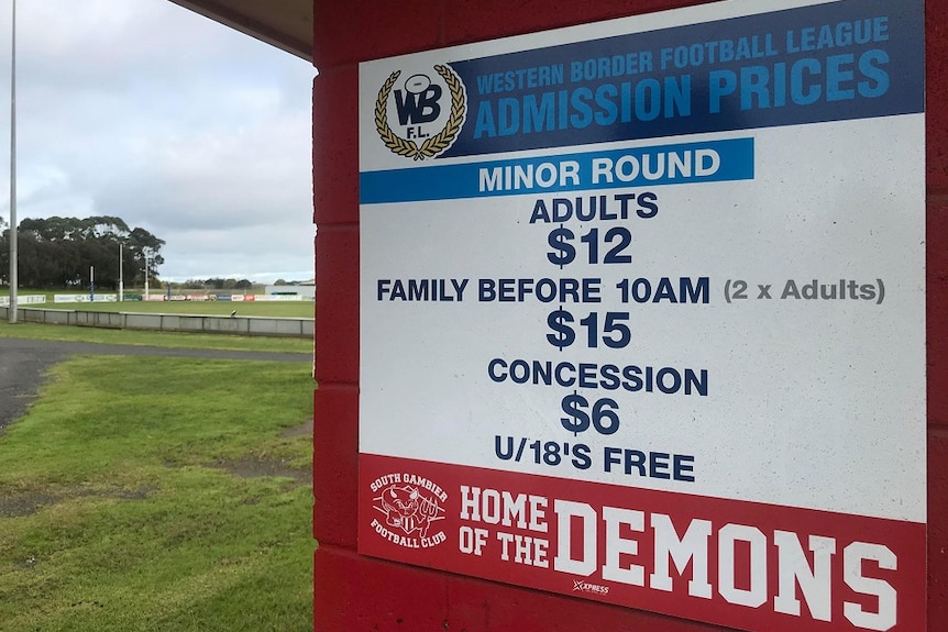 A sign listing entrance costs in front of a footy oval