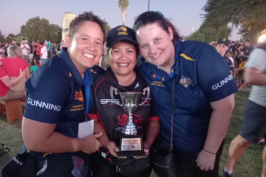Three women smile as they hold up a trophy.