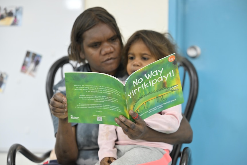 A woman with a little girl on her lap read a book together
