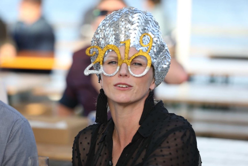 A woman wearing a silver sequinned turban and a pair of novelty glasses shaped to read "2019".