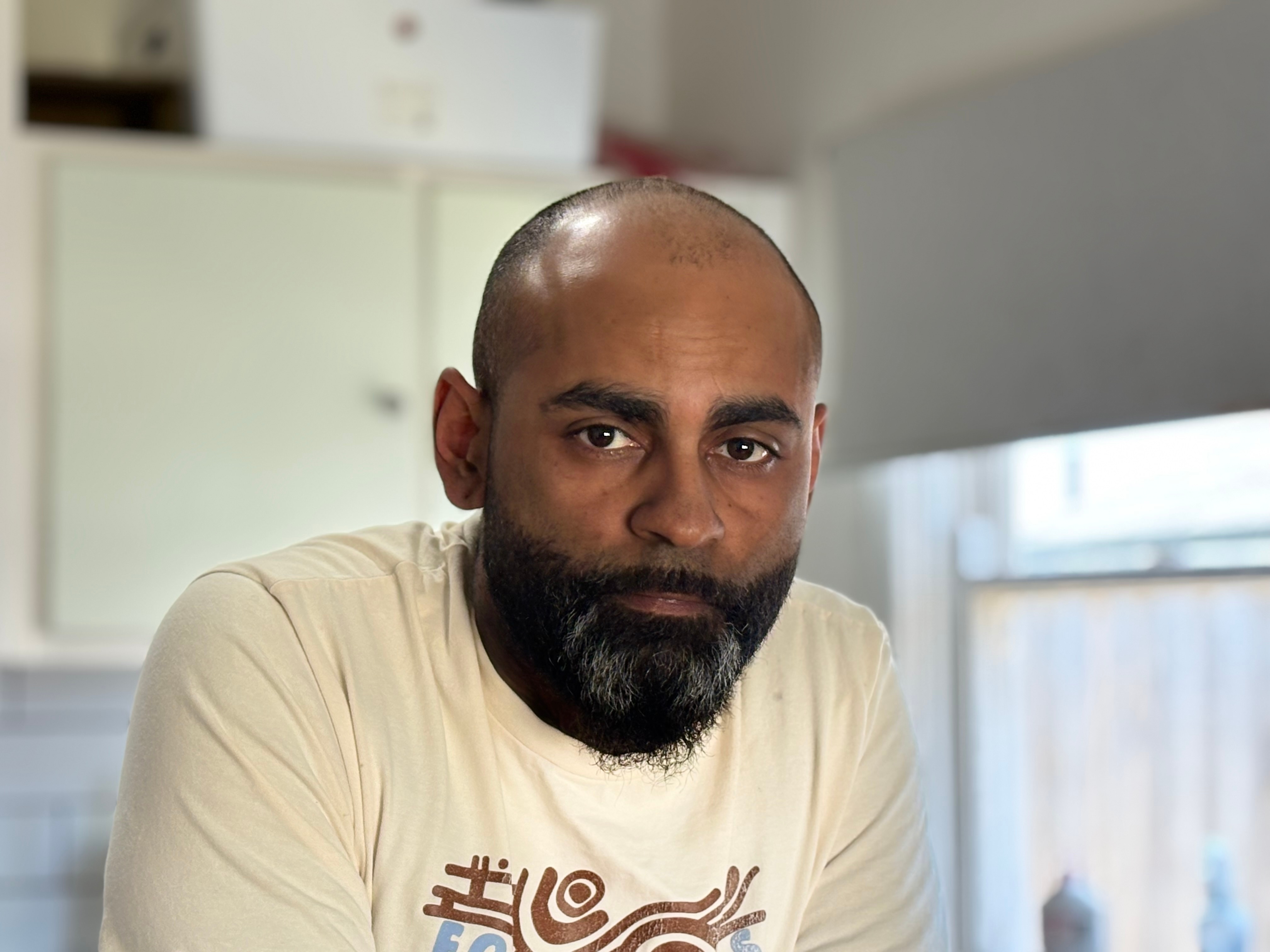 Um indígena olha para a câmera em uma cozinha. 