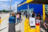 People queue outside the store, wearing masks.