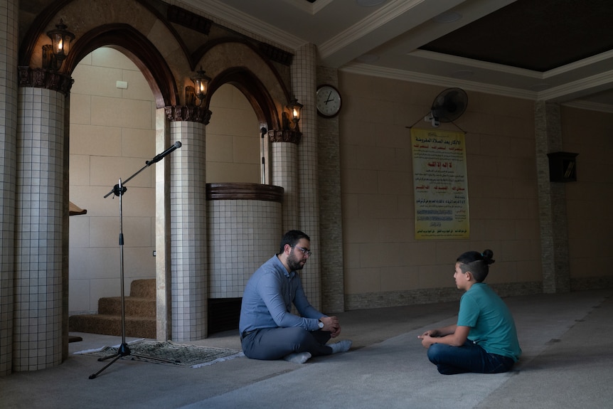 A young boy sits with a man in a mosque.