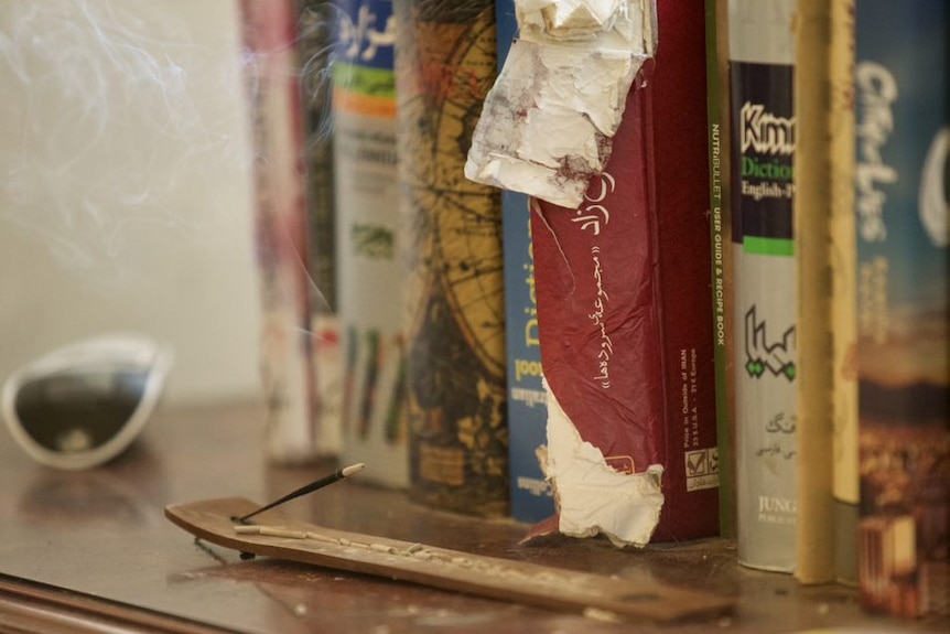 Some books sit on a shelf behind a stick of burning incense.
