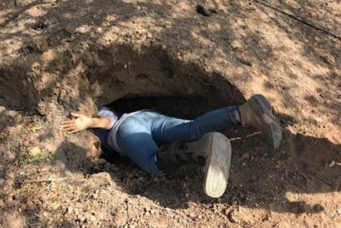 A rescuer wearing jeans and hiking boots with the top half of their body in a large hole in the dirt.