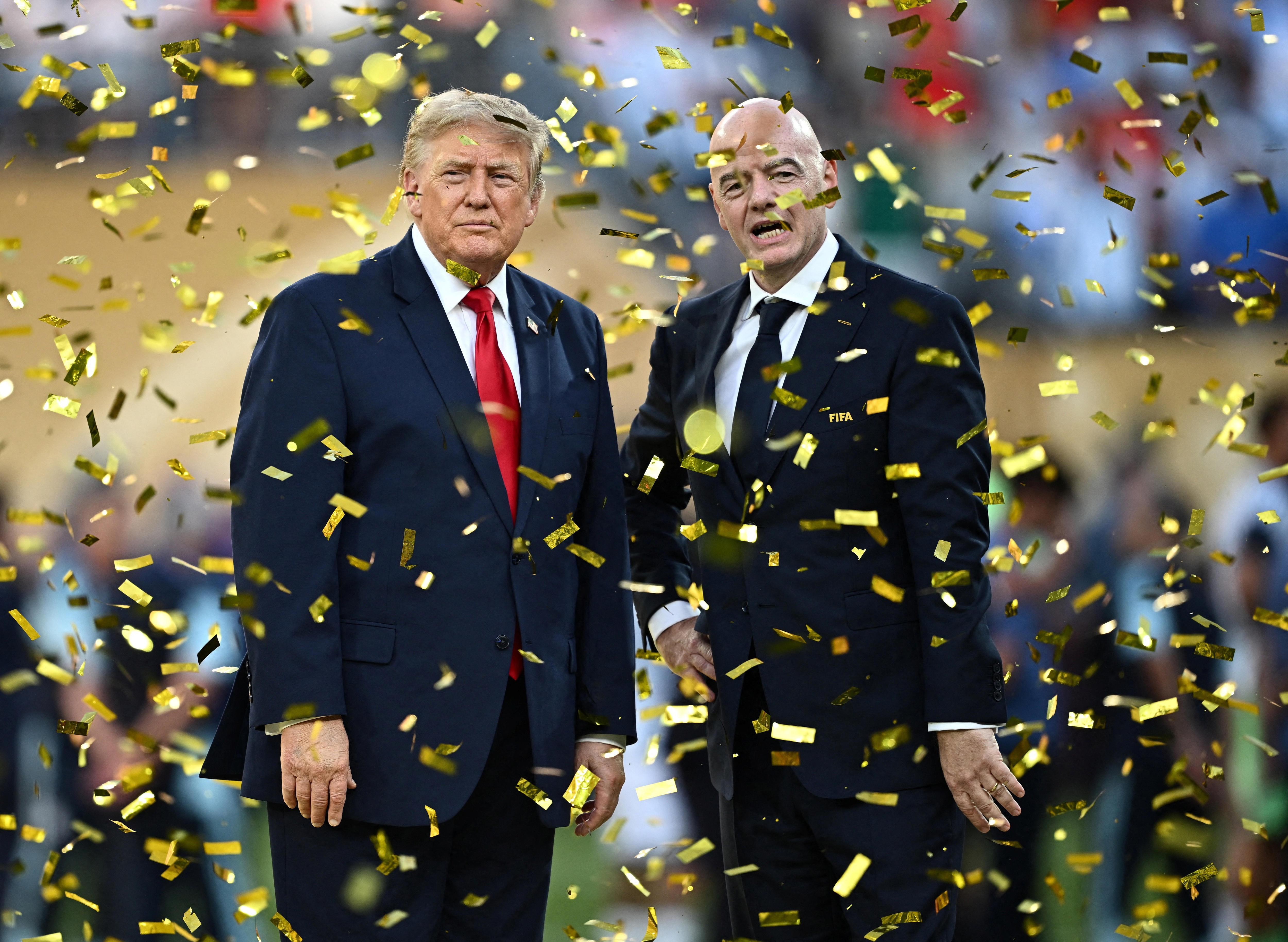 Donald Trump and Gianni Infantino standing while wearing suits amid falling goldens trips of confetti.