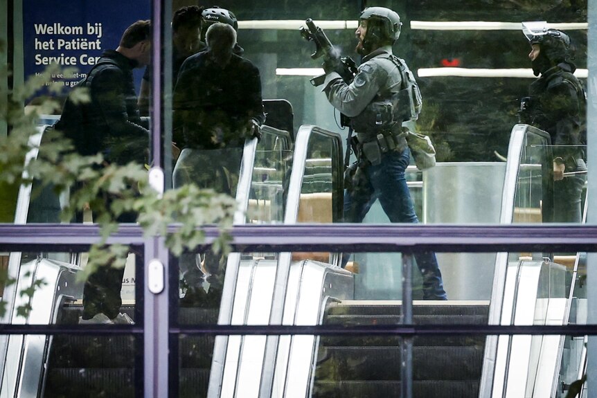 Armed Dutch police walk through a hospital corridor.