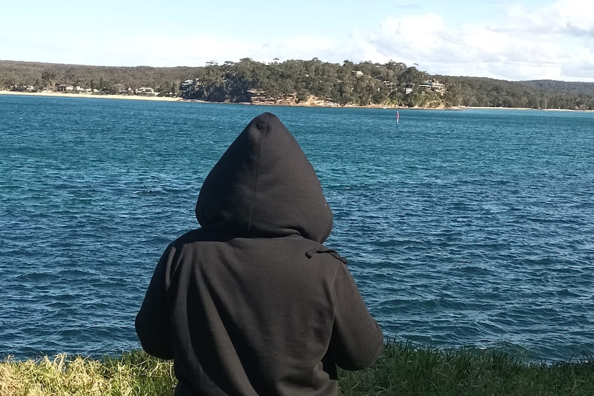 Woman wearing a black hoodie with her back to the camera staring into the open sea.
