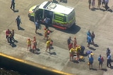 Lifeguards and lifesavers stand nearby an ambulance vehicle as police officers monitor the scene.