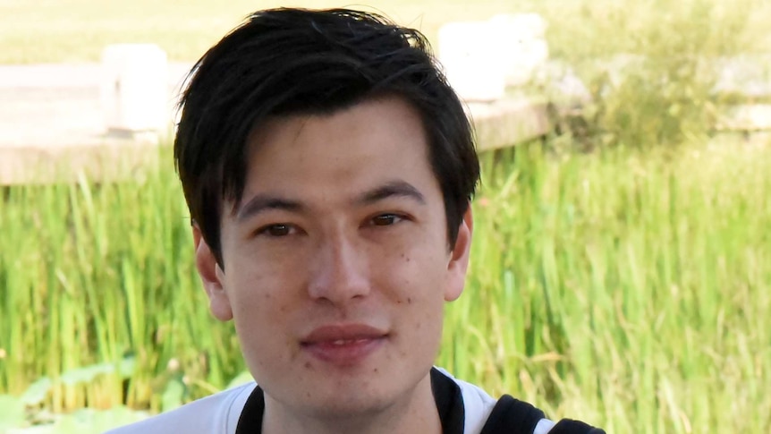 Mid shot of a young man wearing a white t-shirt with a camera slung across his body