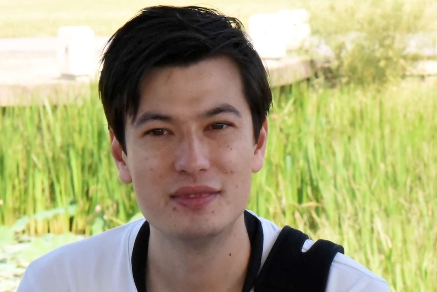 Mid shot of a young man wearing a white t-shirt with a camera slung across his body