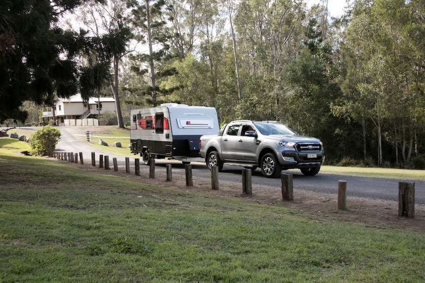 A car towing a caravan on a back road surrounded by greenery on all side. 