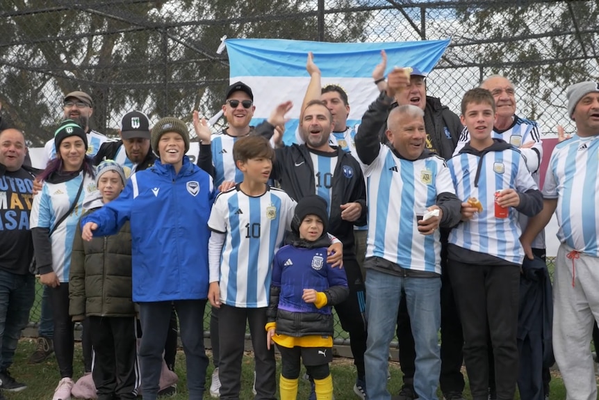 A large group of people wearing Argentina football jerseys cheer and smile