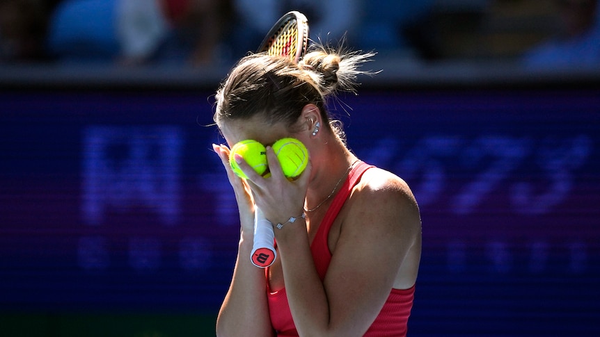 A Ukrainian tennis player stands with her face covered by tennis balls during a match at the Australian Open.