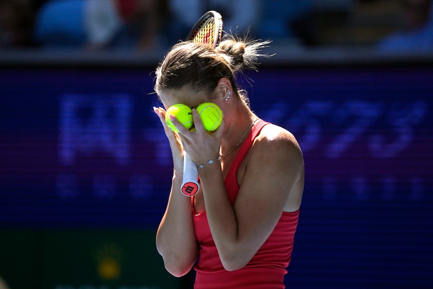 A Ukrainian tennis player stands with her face covered by tennis balls during a match at the Australian Open.