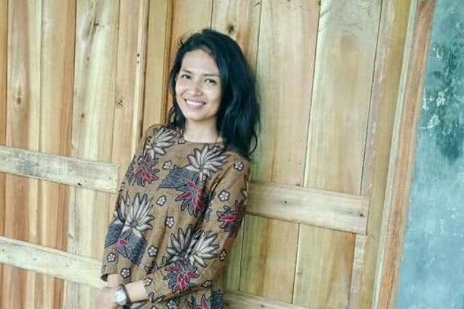 A woman with shoulder length black hair leaning against a wooden door.