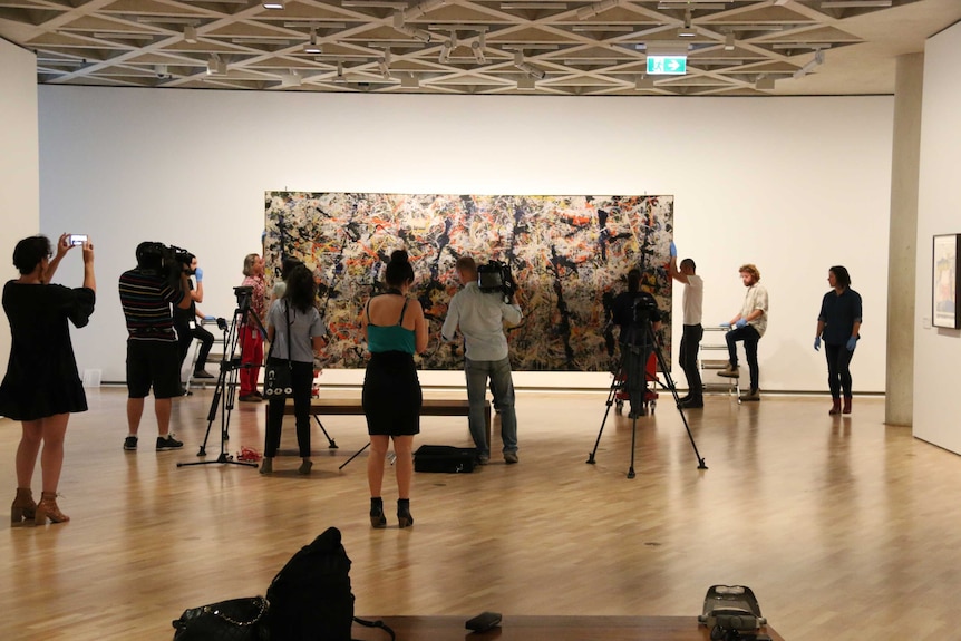 Media and gallery staff stand in front of the Blue Poles artwork to watch it being rehung at the National Gallery of Australia.