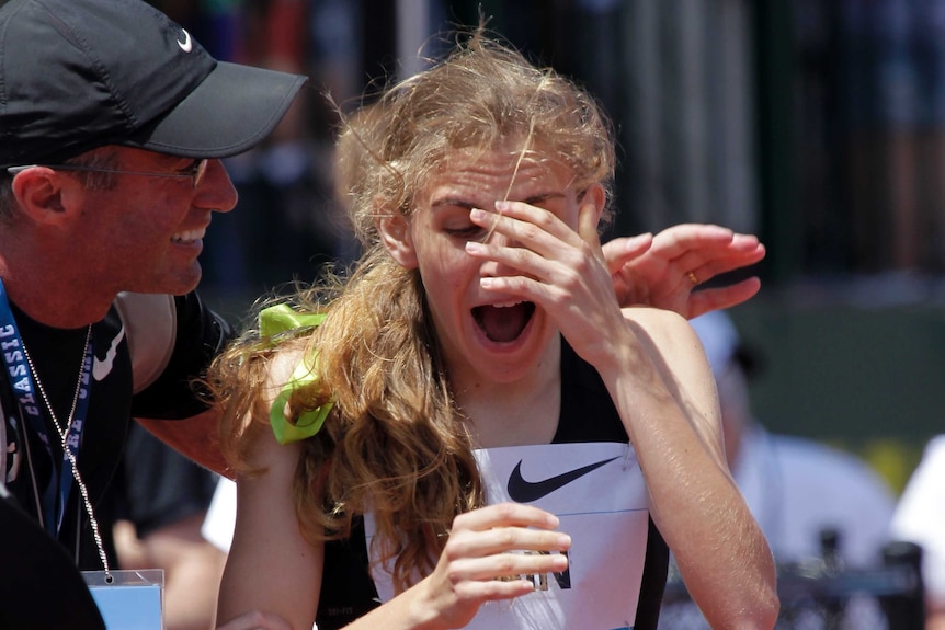 Mary Cain holds her hand to her head and smiles in celebration. Alberto Salazar smiles and puts a hand on her shoulder.