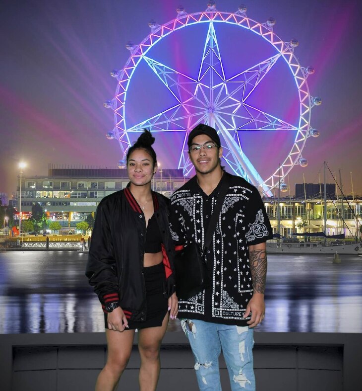 Woman and man smiling at camera in front of wheel