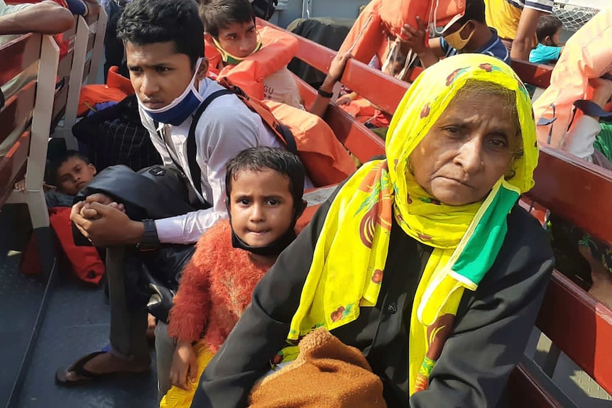 Woman looks worried at front of boat, two young boys and a toddler are behind her.
