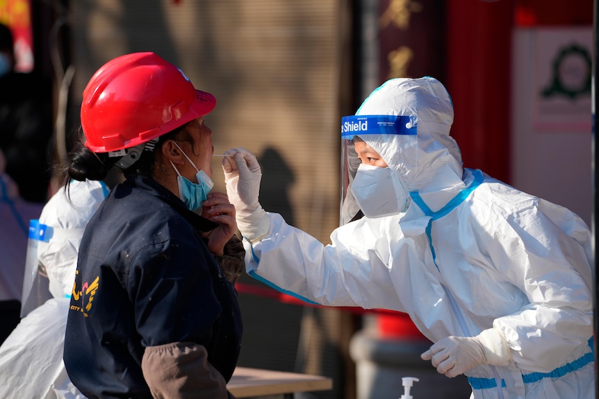 一名身穿防护服的工人在西安 COVID-19 检测点采集咽拭子样本。