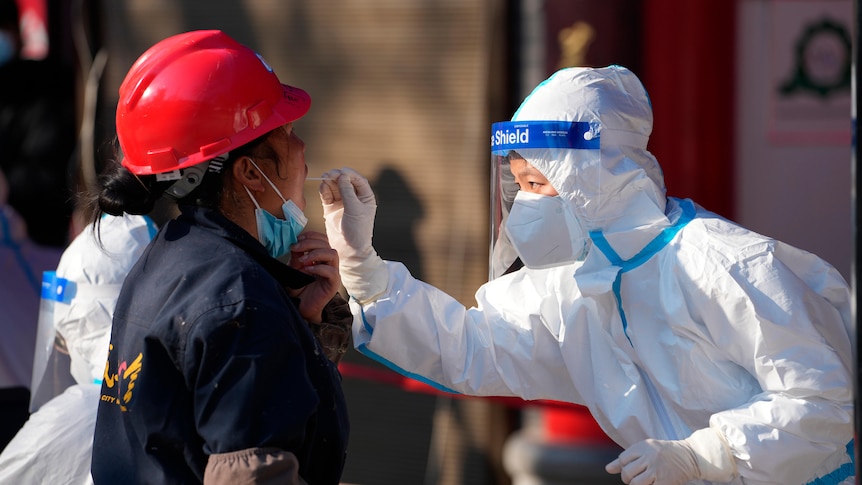 A worker wearing a protective suit collects a throat swab sample at a COVID-19 testing site in Xi'an.