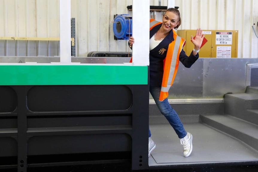 Anne Aly smiles and waves while wearing a high-vis jacket and sneakers