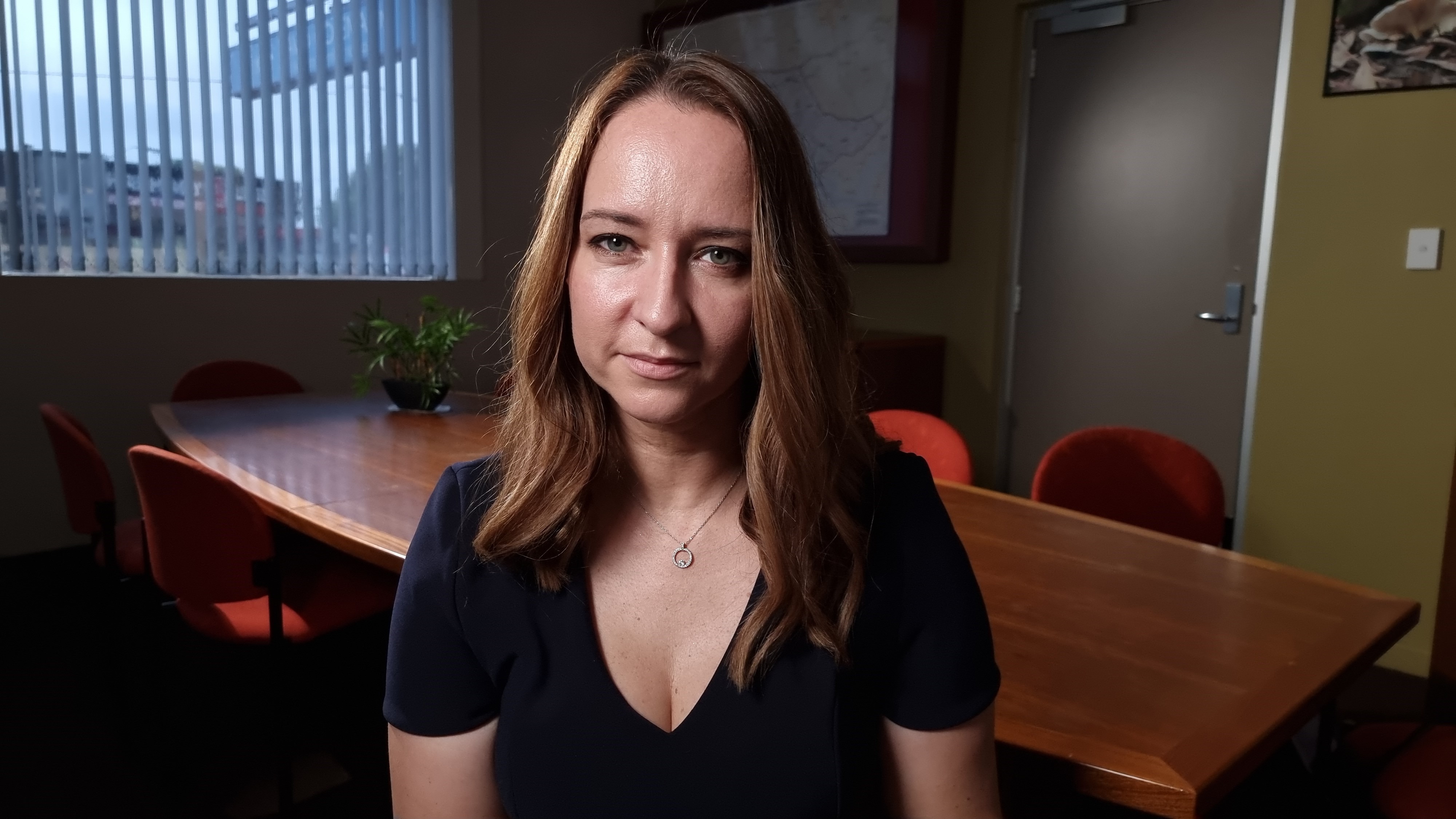 A woman wearing a dark t-shirt looking at the camera. 