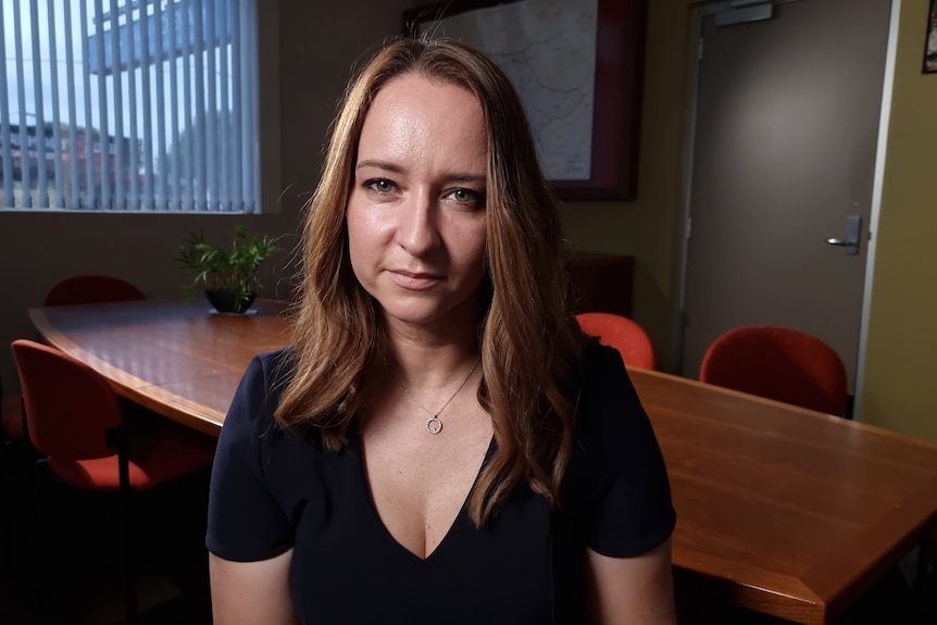 A woman wearing a dark t-shirt looking at the camera. 