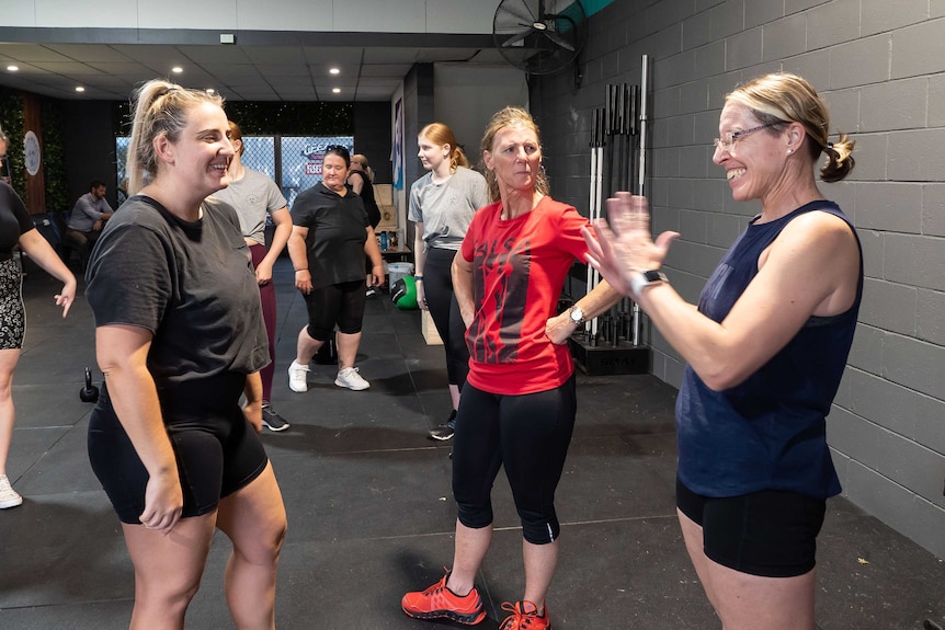 A group of woman who are deaf and hard or hearing stand in a gym having a conversation in Auslan.