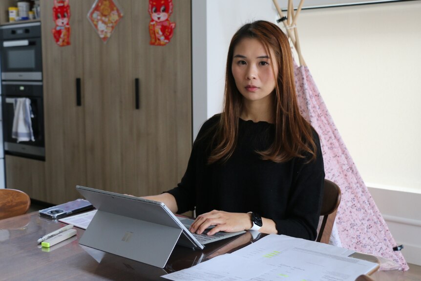 A young woman of Asian background sitting at a table with a laptop