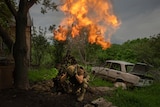 A Ukrainian soldier covers his ears as he fires a mortar at Russian positions next to a burnt out car.