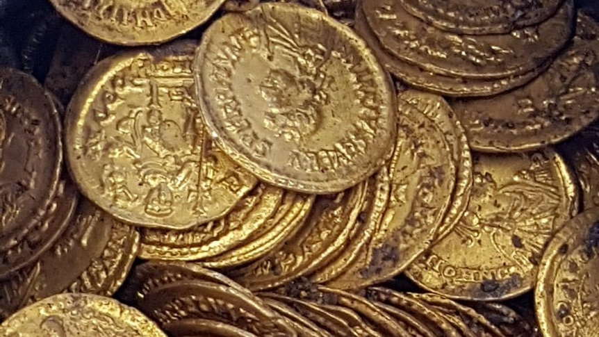 A close up photo of bright gold ancient coins. They are engraved with a bust and text in a very similar way to modern coins