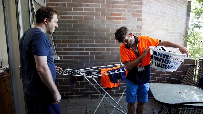 A man stands next to a clothes drying rack on a balcony while another holds a washing basket for a story on share housing.