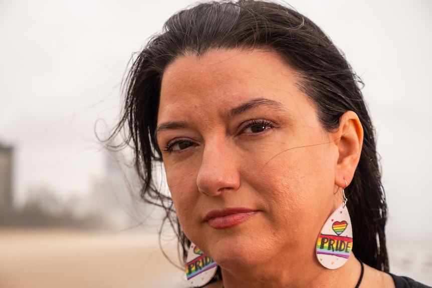 A dark-haired woman wearing large earrings that say "Pride".