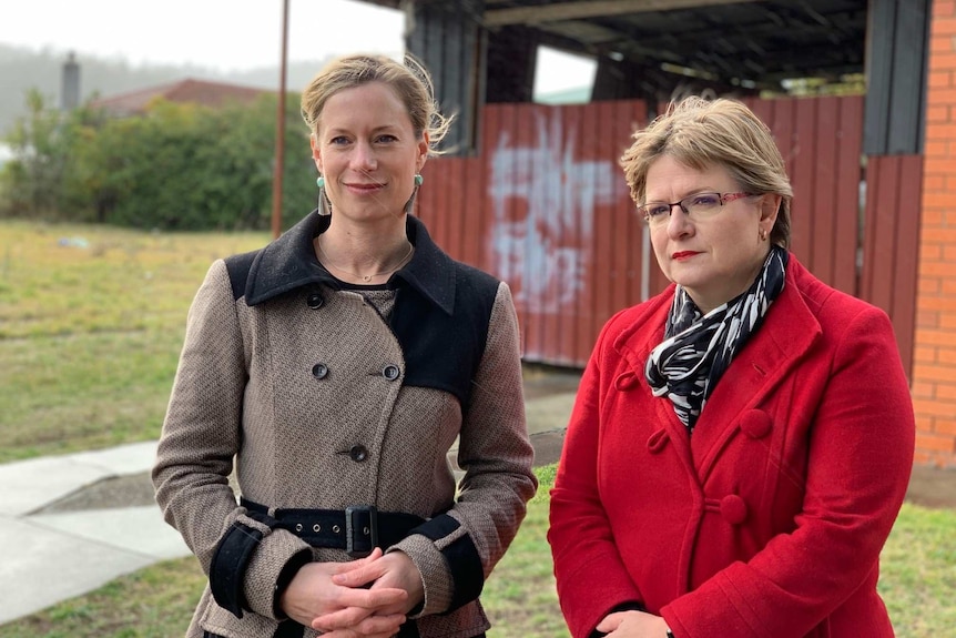 Two women stand outside a rundown house.