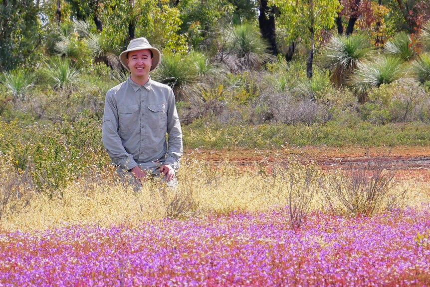A man wearing a hat stands in a field of flowers.