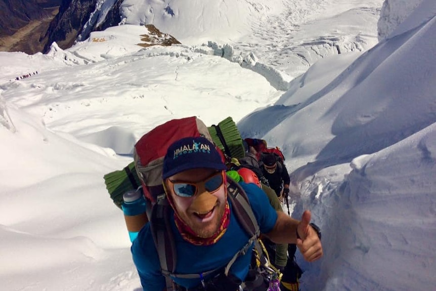 Man in sunglasses and nose protector climbing snowy moutain.