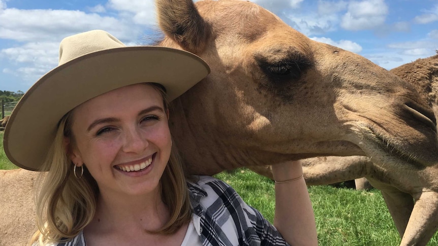 Camel farmer Yasmin Brisbane from Q Camel, smiles as she embraces one of her camels in a paddock.