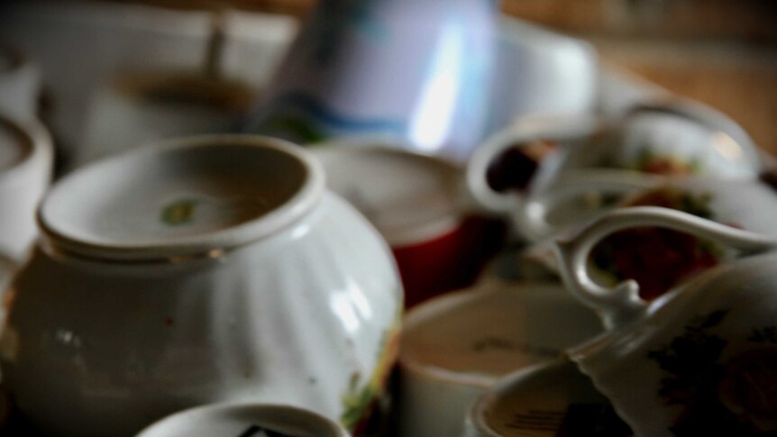 A pile of old tea cups are stacked messily in a box, the focus is soft.