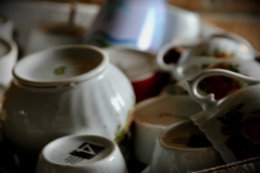 A pile of old tea cups are stacked messily in a box, the focus is soft.