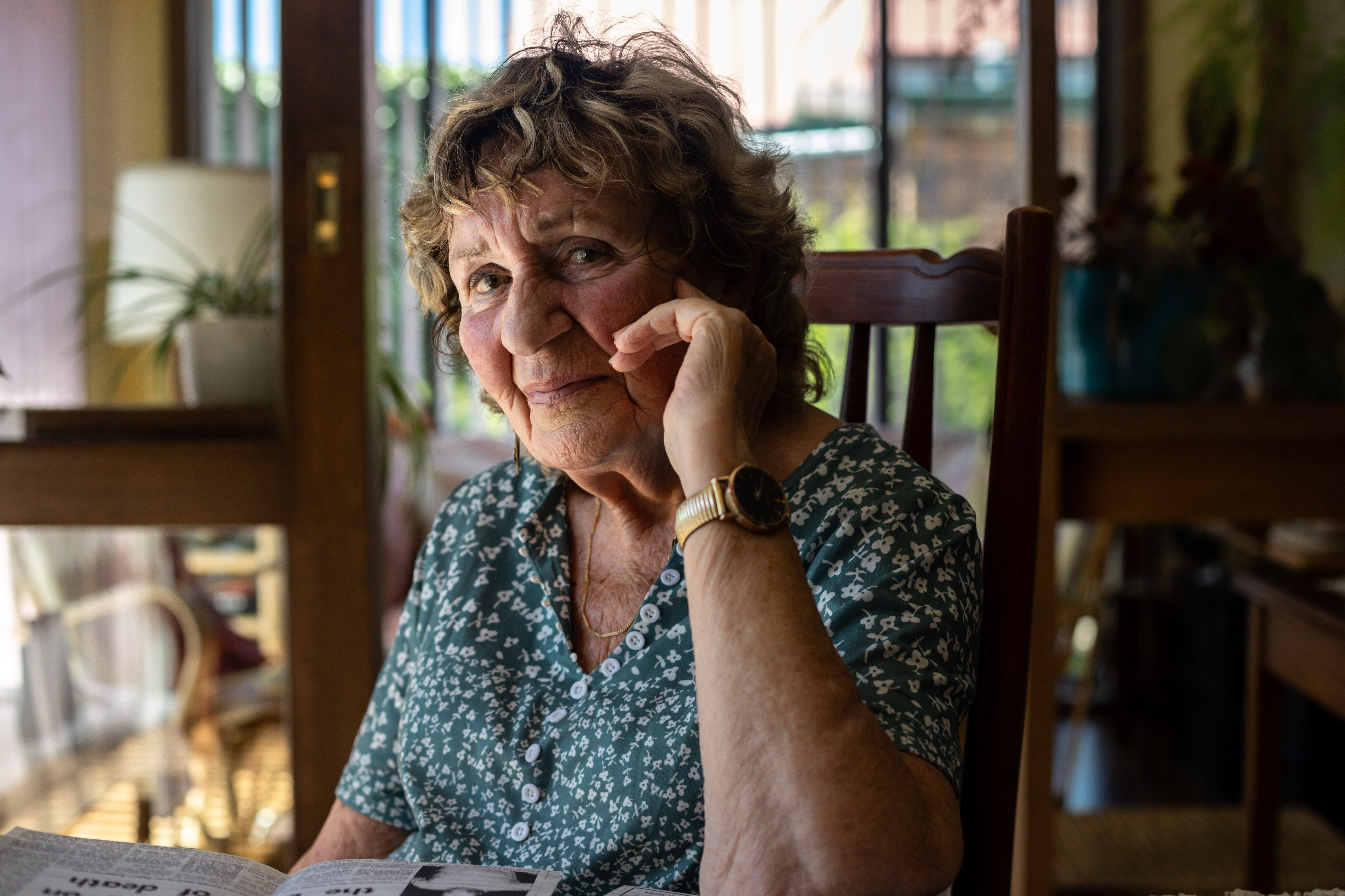 An 80 year old lady in a green top poses for a photo.