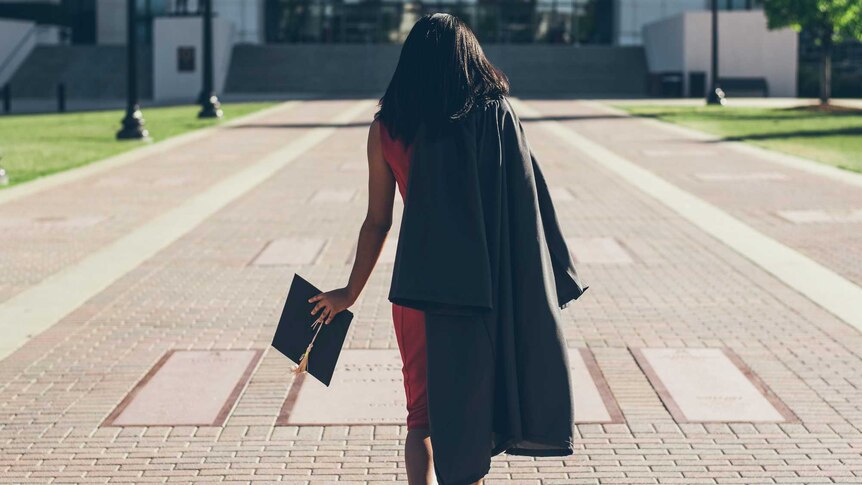 A woman walks away in a graduation cap and gown