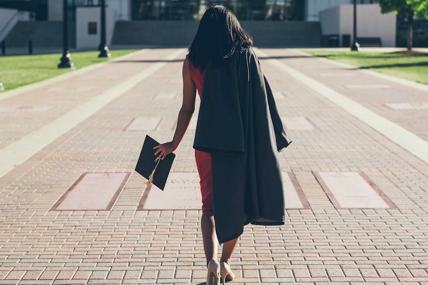 A woman walks away in a graduation cap and gown