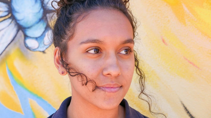 A young Indigenous girl smiles softly looking to the left of the camera.