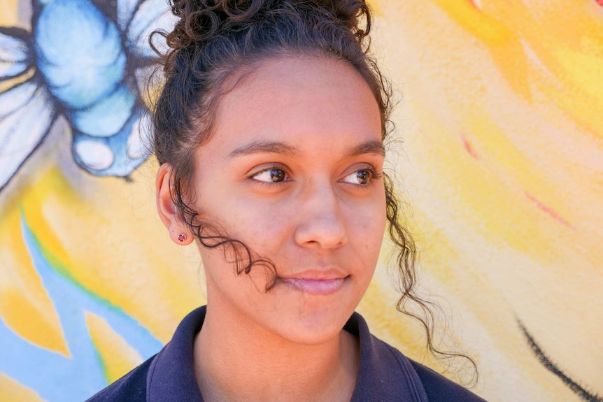 A young Indigenous girl smiles softly looking to the left of the camera.