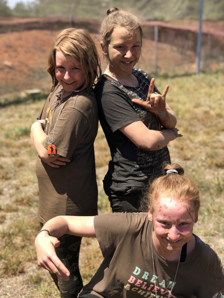 Three teenagers pose, covered in mud. All are smiling.