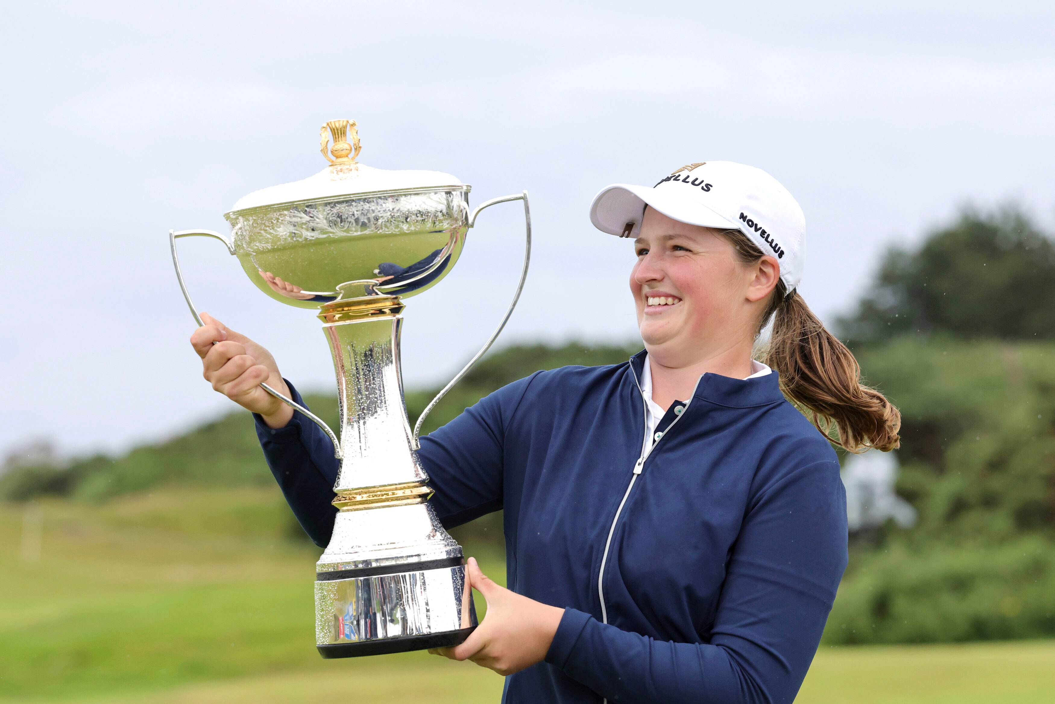 A golfer grins as she stands holding a trophy after winning a tournament.